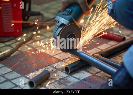 Male hand cuts off pieces of water pipe with angle grinder Stock Photo