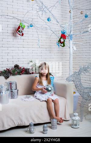 Little girl sitting on the sofa with Christmas gifts and mirror ball Stock Photo