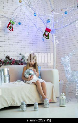 Little girl sitting on the sofa with Christmas gifts and playing with a mirror ball Stock Photo