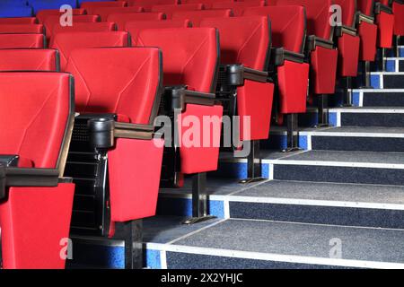 Rows of red seats and grey stairs in auditorium in cinema theater. Stock Photo