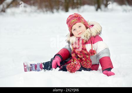 Little girl sits on snow in winter park Stock Photo
