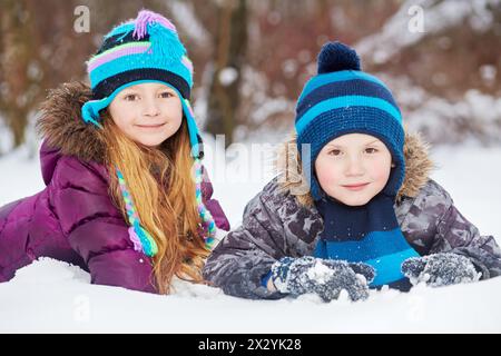 Smiling little girl and boy lie side by side on snowdrift in winter park Stock Photo
