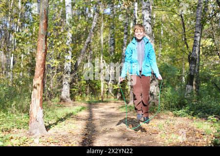 Happy boy jumps with skipping rope in forest on sunny day. Stock Photo
