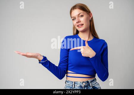 Woman in Blue Top Pointing With Hand Against Neutral Background Stock Photo