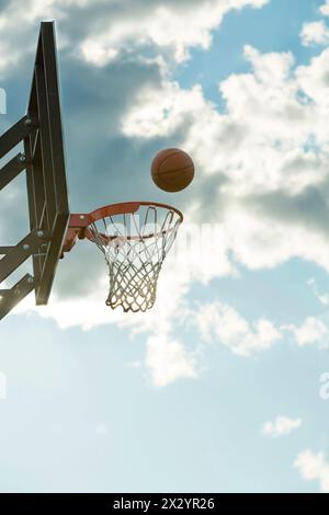 The ball flies into the basketball against the sky and clouds Stock Photo