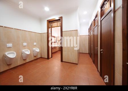 Light and clean public toilet with urinals, red tiles and wooden doors. Stock Photo