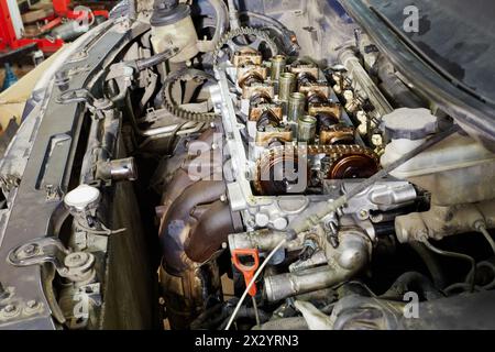 Four-cylinder car engine with cover off under open car hood Stock Photo