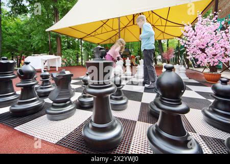 Big chess pieces on chessboard in park and chindren moving chess pieces. Focus on chess. Stock Photo