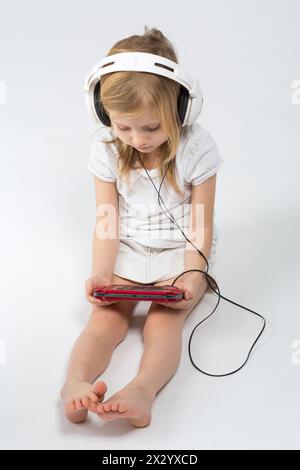Barefoot girl sitting in big headphones with a gaming device in the hands Stock Photo