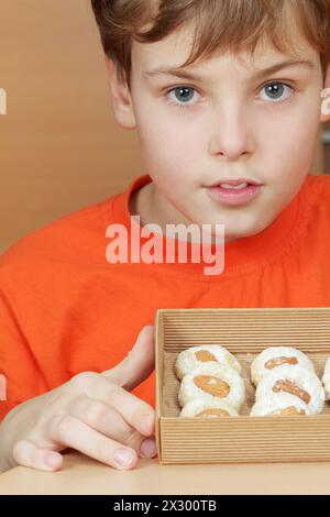 Boy in orange t-shirt holds open box of corrugated cardboard with cookies with almonds and icing sugar Stock Photo
