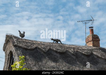 Animal finials on a thatched roof, a cat chasing a hen, and a traditional brick chimney. Great Shelford, Cambridgeshire, England, UK Stock Photo