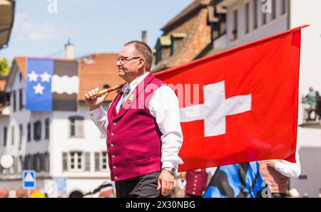 Ein Mann in traditioneller Schweizer Tracht steht mit einer Schweizer Fahne während dem Festumzug des Jodelfests in der Bad Zurzacher Altstadt. (Bad Z Stock Photo