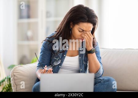 Overworked African American Woman Sitting on Couch With Laptop Stock Photo