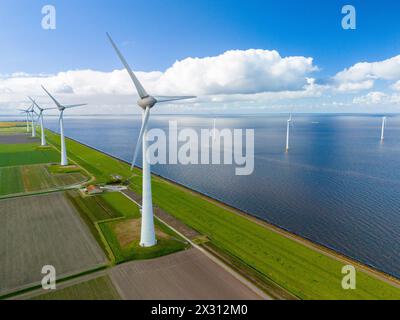 A wind farm generates clean energy in the middle of a vast Dutch lake, with rows of windmill turbines spinning gracefully under the spring sky. Ijsselmeer windmill turbines Noordoostpolder Netherlands Stock Photo