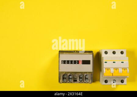 Electricity meter and automatic switch circuit breaker close up on the yellow flat lay background. Stock Photo