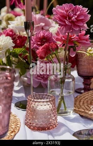 Romantic table arrangement with candle and vibrant flowers. Table aesthetics and design, summer picnic party. Stock Photo