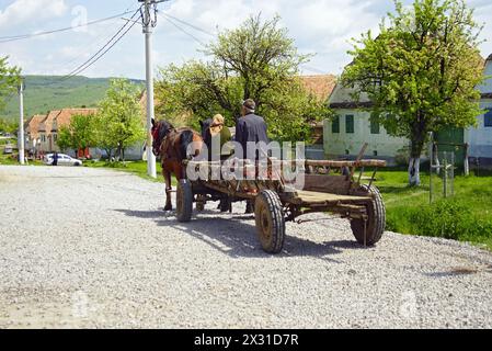 An elderly couple riding in a horse-drawn cart along the road in the Romanian village of Viscri Stock Photo