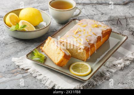 Homemade glazed lemon pound cake closeup on the plate served with tea on the table. Horizontal Stock Photo