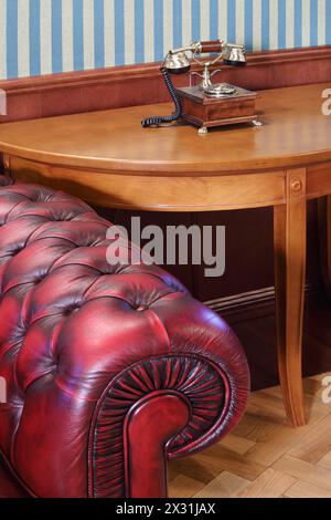 Part of red leather armchair and vintage phone on wooden table. Stock Photo