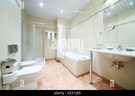 Light and empty bathroom with white bath, toilet and shower cabin. Stock Photo