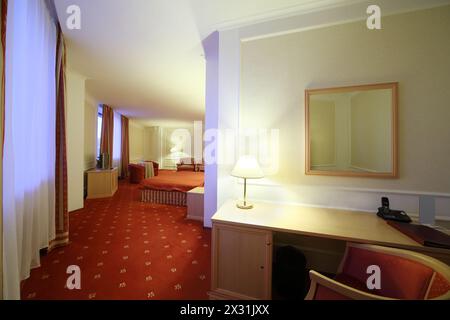 Table and chair in stylish room with double bed with red linen and red carpet. Stock Photo