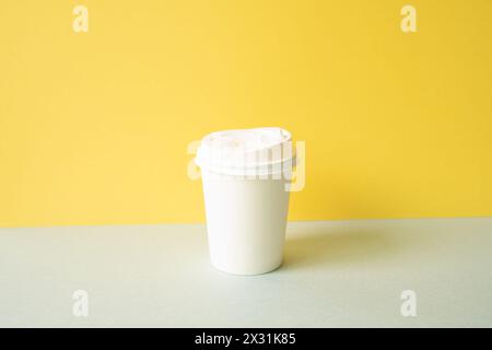 Disposable paper coffee cup on gray table. yellow wall background Stock Photo