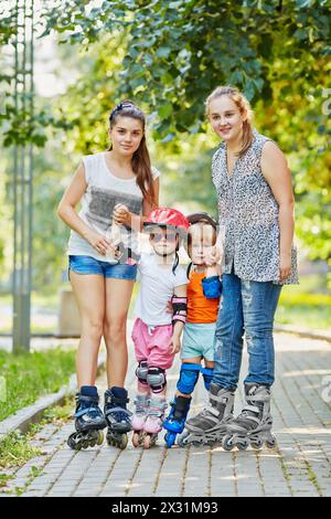 Two teenage girls and two kids in rollers stand together on walkway in park Stock Photo