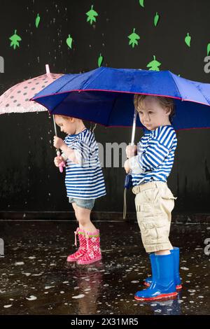 Little girl and boy in a striped vest under a blue and pink umbrellas, focus on the boy Stock Photo