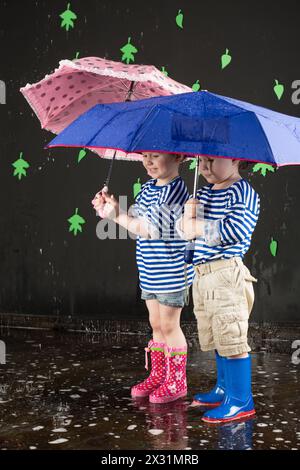 Little girl and boy in a striped vest under a blue and pink umbrellas Stock Photo