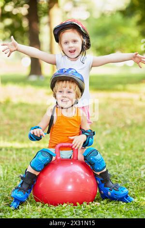 Little boy sits on red ball for jumping, girl stands behind him with her arms outstretched to sides Stock Photo