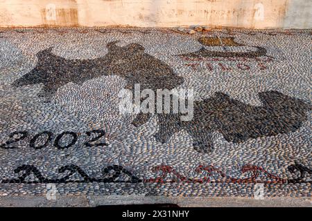 Pebble mosaic with the shape of Tilos island, the date 2002 and an ancient trireme in black pebbles, at the port of Livadia town, Tilos, Greece,Europe Stock Photo