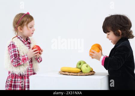 Little boy and girl stand and hold fruits on white background. Stock Photo