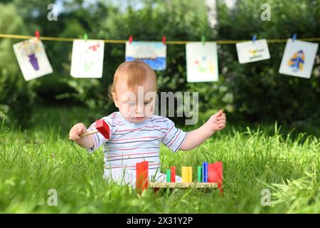 A little boy is playing with colorful wooden toys on the grass, in the background hanging kids drawings Stock Photo