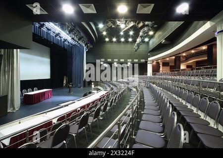 Rows of black chairs and stage in big black hall for business meetings. Stock Photo