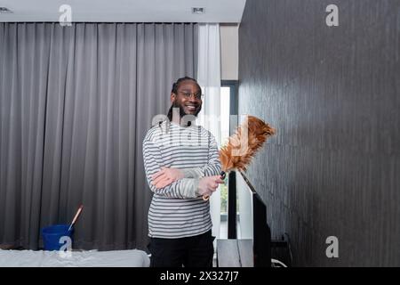 Young African American man for cleaning apartment, holding mop and other cleaning tools. Cheerful african american man housekeeping on weekend Stock Photo