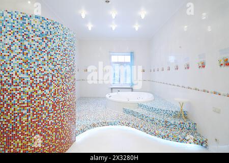 Round clean jacuzzi and stairs in spacious white bathroom with tiles with poppies. Stock Photo