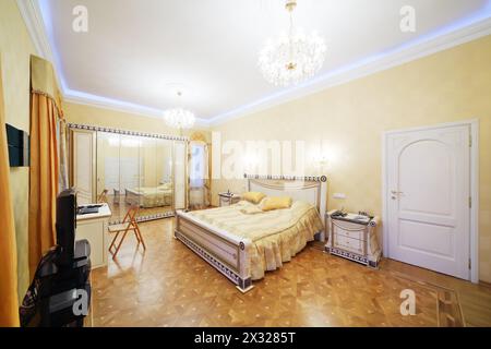 Bedroom with beautiful bed, tv, mirrorlike wardrobe in classic style. Stock Photo