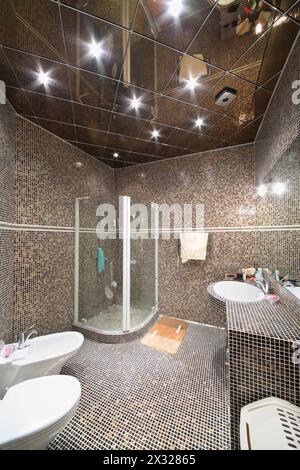 Bathroom with shower cabin, toilet and bidet with small black and brown tiles. Stock Photo