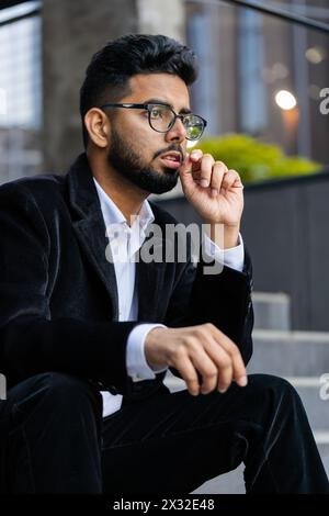 Unhappy sad Indian business man frustrated stress pensive feeling bad after company unemployment lost job problem solution crisis outdoor. Arabian Hindu freelancer guy sitting on stairs downtown city Stock Photo