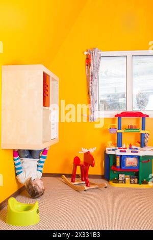 Little girl in children room sitting at the shelves upside down at inverted house Stock Photo