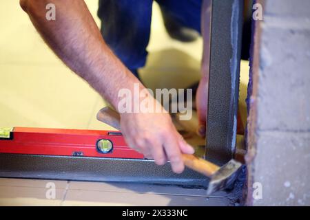 Hand of builder with hammer inserting door frame to aperture in unfinished apartment. Stock Photo