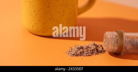 Cinnamon spilled out of a tube in front of a yellow mug on an orange background Stock Photo