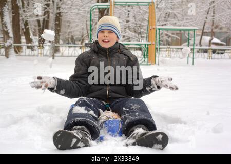 laughing boy sits in a snowdrift and plays snowballs Stock Photo