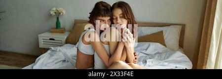 Intimate moment with two women in casual attire sitting on bed. Stock Photo