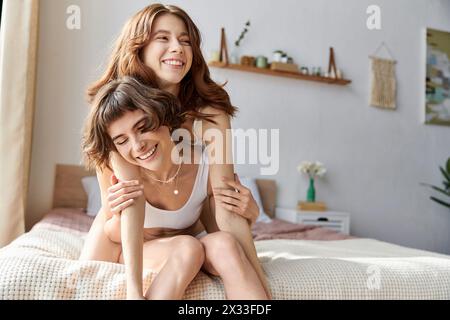 Two women in cozy attire share a tender moment on a bed. Stock Photo