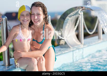 mother and daughter sitting on the edge of the rooftop swimming pool Stock Photo