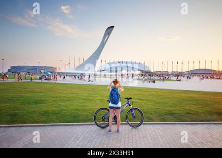 SOCHI, RUSSIA - JUL 27, 2014: Tourists walk in the Olympic park with a bowl of the Olympic flame and the stadium Fischt Stock Photo