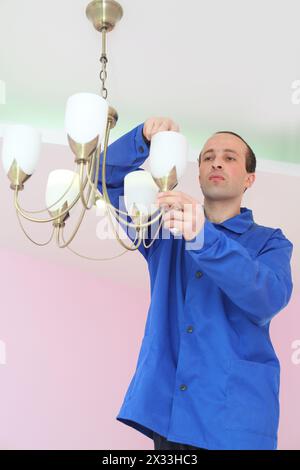 Electrician twists bulb in the chandelier on the ceiling Stock Photo