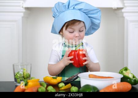Little girl in kitchen apron and cap with large red pepper Stock Photo