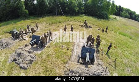 RUSSIA, MOSCOW - JUL 12, 2014: Soldiers in uniform of Soviet Army of World War II stand near three guns on battle field at spring sunny day. Aerial vi Stock Photo